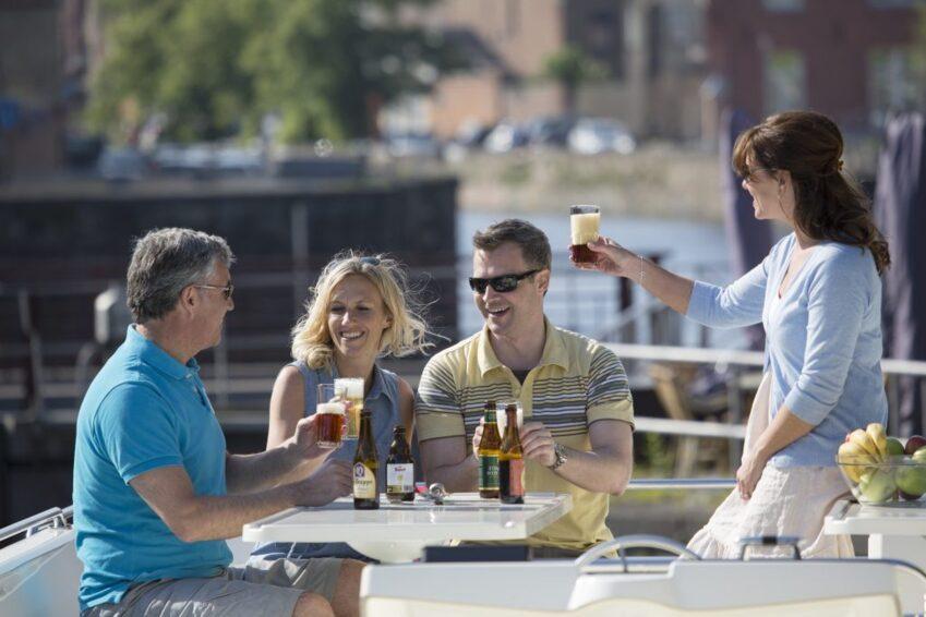BELGIUM 12 1024x683 1 Un grupo de amigos brindando con cerveza en la cubierta exterior de un barco fluvial en Bélgica.
